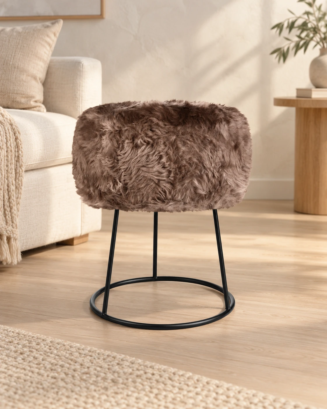 Brown Taupe sheepskin stool with a black circular metal base in a light living room with cream upholstered furniture