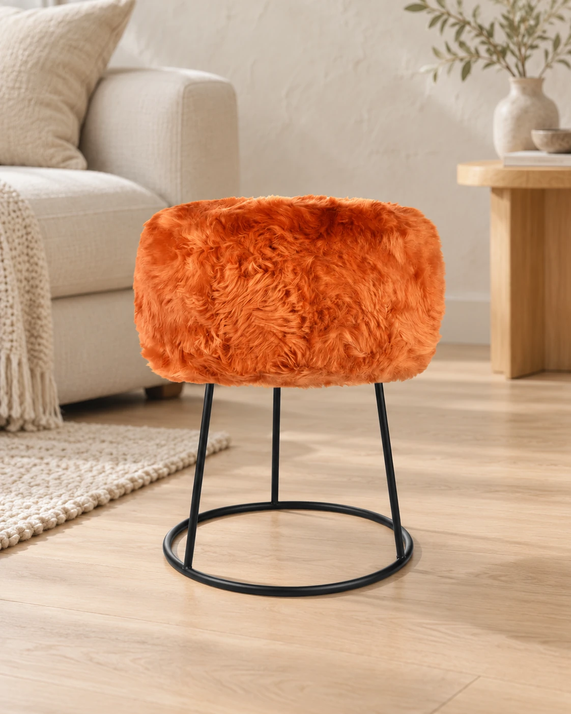 Sunset Orange sheepskin stool with a black circular metal base in a light living room with cream upholstered furniture